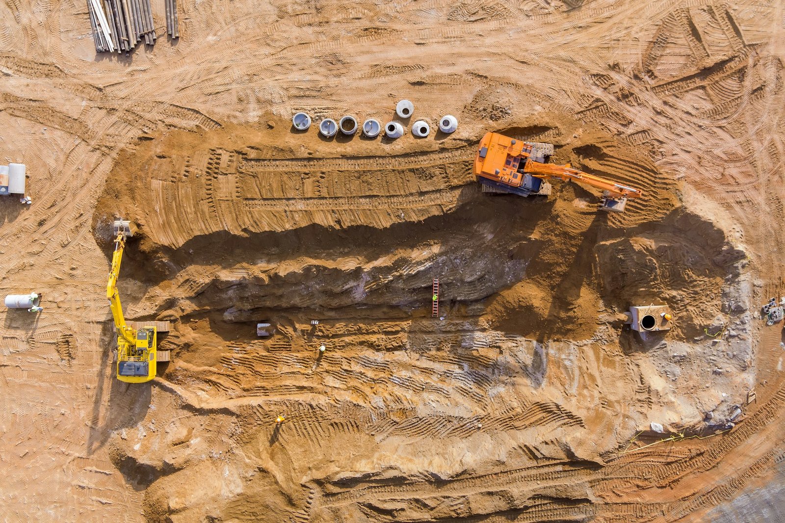 On the construction site, an excavator digs a pit in preparation for the installation of sewer lines